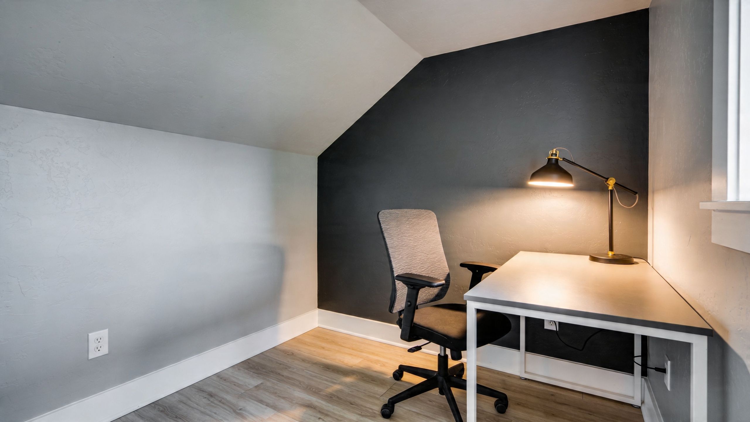 A modern home office setup featuring a desk, chair, and desk lamp against a dark accent wall.