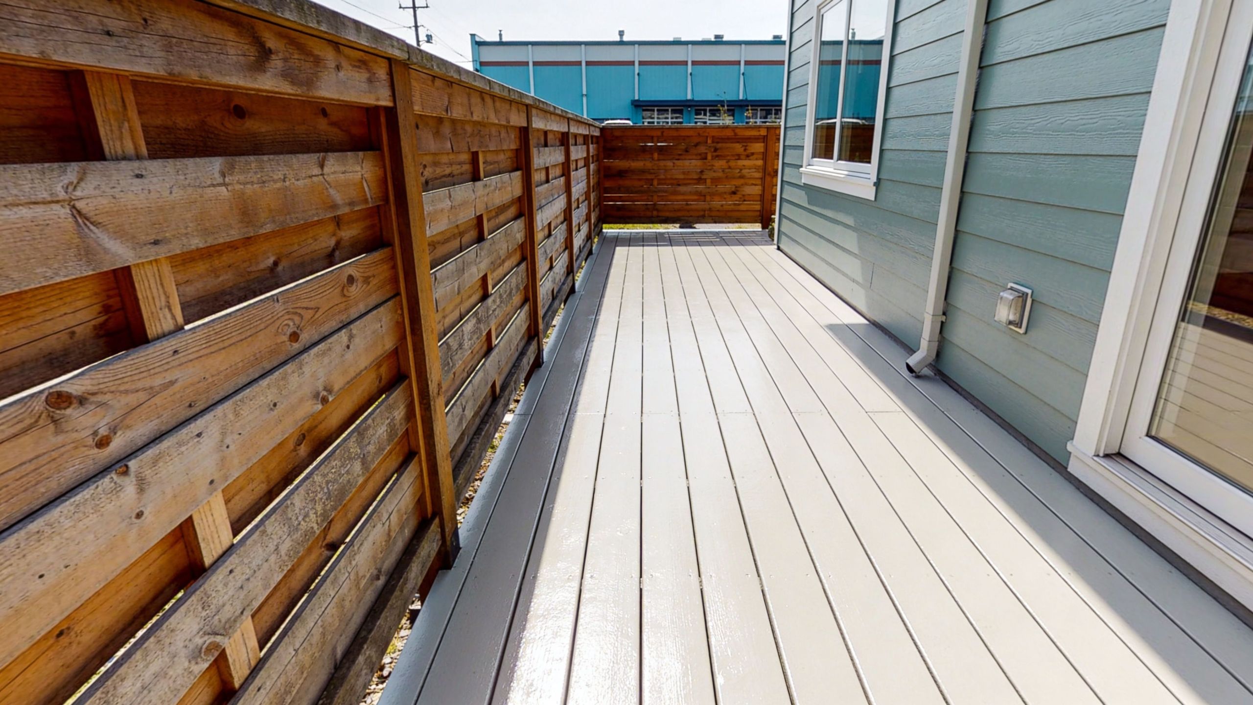 A modern outdoor balcony deck featuring painted light gray floorboards next to a wooden privacy fence.